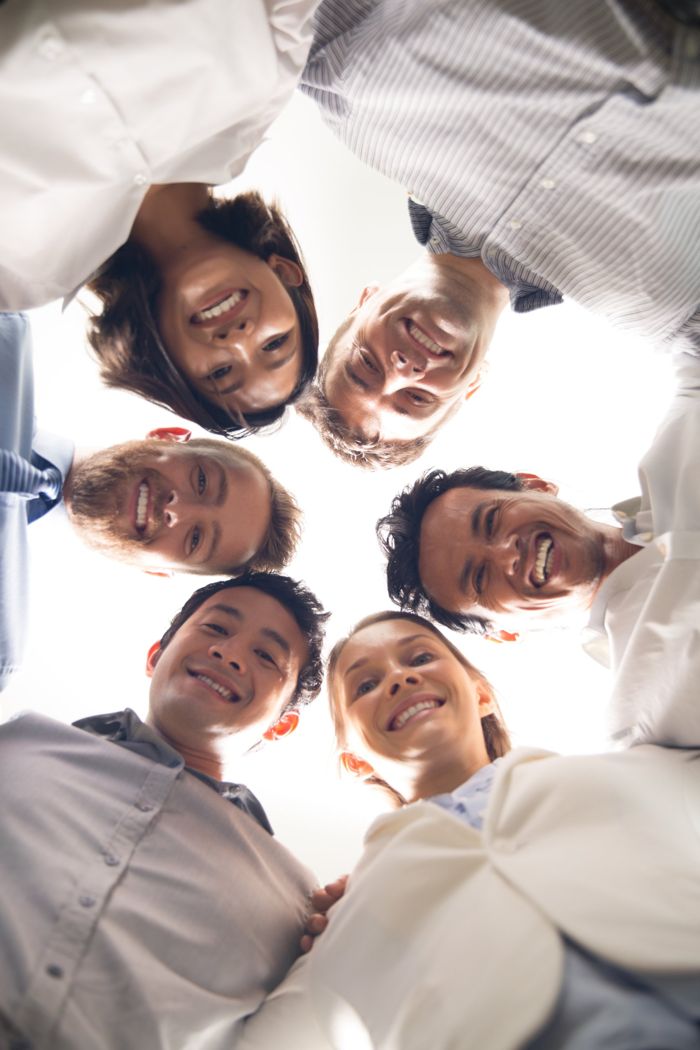 Un gruppo di colleghi sorridenti in cerchio, ripresi dal basso